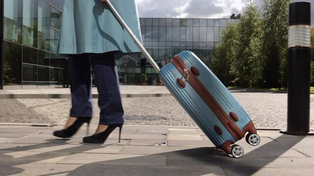 Businesswoman with suitcase in hand walking along city during business trip spbi. Closeup view of young woman moves luggage and walks on street along glass building on autumn day. One millennial