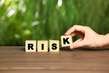 Woman making word Risk of cubes on wooden table, closeup