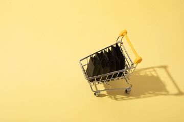 Miniature supermarket cart with shopping bags in black friday sale on yellow background