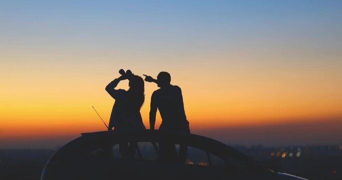Couple stargazing together with binoculars from a car's roof on a countryside suburban area.