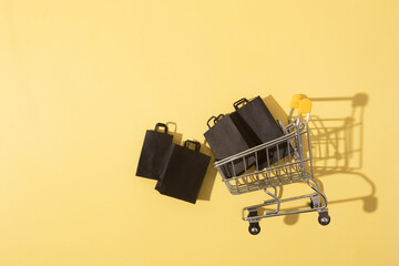 Flat lay miniature supermarket cart with shopping bags in black friday sale on yellow background