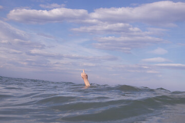 Person submerged on a beach with the hand out making a comb, clenching the fist and raising the middle finger