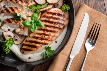 Roasted chicken fillet and mushrooms with herb in the frying pan on the wooden table close-up.