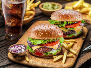 Delicious cheeseburger with cola and potato fries on the wooden background. Fast food concept.