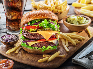 Delicious cheeseburger with cola and potato fries on the wooden background. Fast food concept.