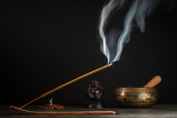 Asian incense stick in stick holder burning with smoke on black background