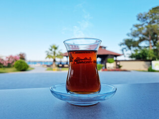 Turkish tea served in tulip-shaped glass on a small saucer blurred nature background. Summer holiday background.
