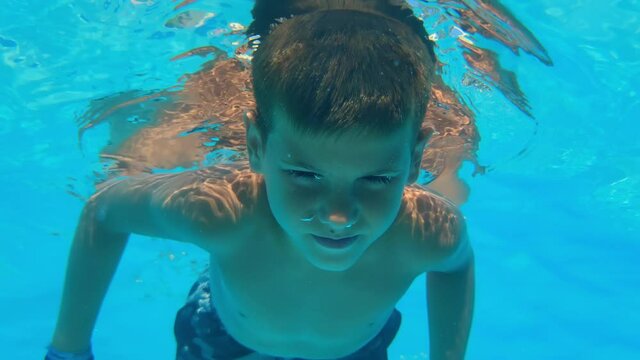 little boy learns to swim under water with open eyes, child swims in the outdoor blue pool during active summer vacation