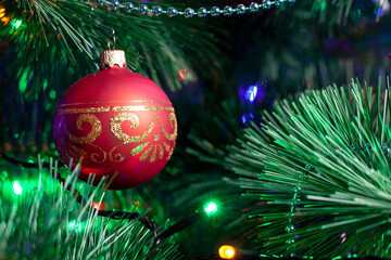 Christmas decoration, red glass ball on a green Christmas tree branch. christmas garland on tree. Shallow depth of field ball with golden ornament. New year background with soft focus