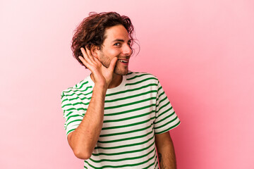 Young caucasian man isolated on pink bakcground trying to listening a gossip.