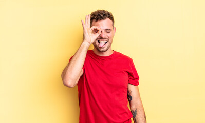 young handsome hispanic man smiling happily with funny face, joking and looking through peephole,...