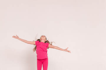 a beautiful girl in a pink jumps and smiles on a white background. happy childhood.