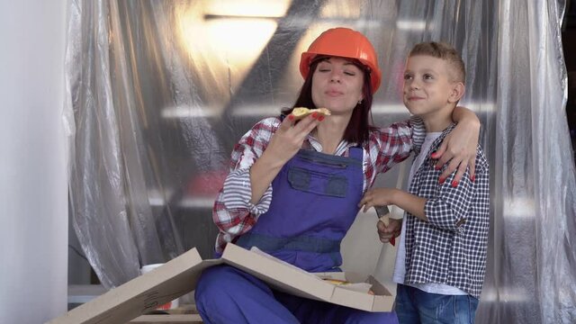 Pretty young woman builder with helmet Working on apartment renovation with her son. Construction, repair and renovation. take a break and eat pizza.