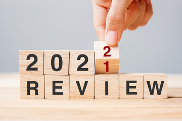 Businessman hand holding wooden cube and flip over block 2021 to 2022 REVIEW on table background. Resolution, goal, change, start and New Year holiday concepts