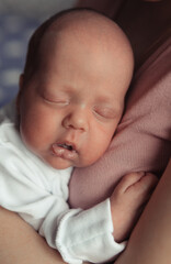 Close-up portrait of newborn baby sleeping on mothers arms. Mother holding tight newborn daughter on her arms. Selective focus. Film grain