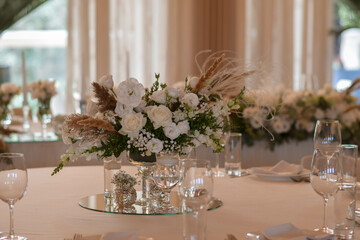 White tablecloths with clear vases and white flowers and fern arrangements. Golden colored plates, peavh napkins, table numbers and mirror centerpieces.