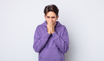 young handsome hispanic man feeling worried, hopeful and religious, praying faithfully with palms...