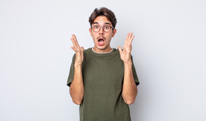 young handsome hispanic man looking shocked and astonished, with jaw dropped in surprise when...