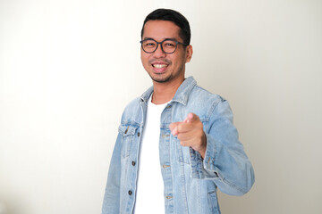 Adult Asian man wearing blue jeans jacket pointing forward while smiling happy