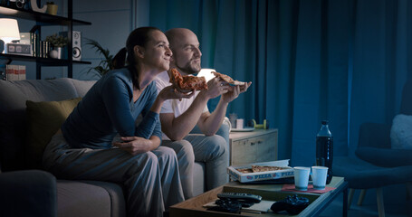 Happy couple sitting on the couch and eating pizza together