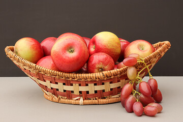 apples and grapes in a wicker wooden basket on the table