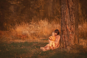 Mom with a baby in a magic forest. Mom hugs her son. Mom and son are sitting by the tree. Autumn forest. Wonderful autumn. A family