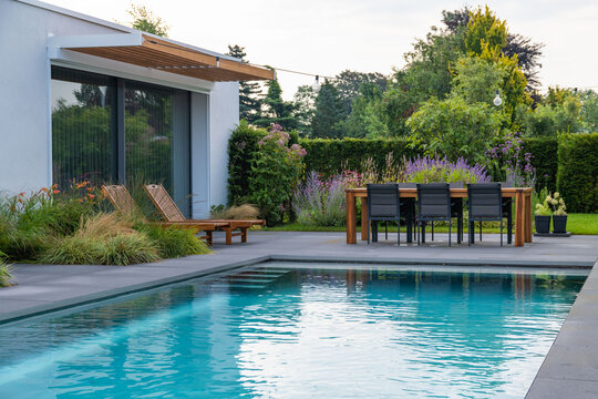 Sunbeds and dining zone near pool in backyard of modern house