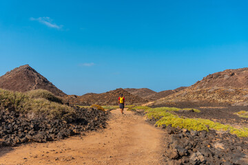 A young man with a yellow backpack on the trail heading north to Isla de Lobos, along the north coast of the island of Fuerteventura, Canary Islands. Spain