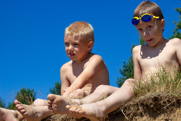 two boys are sitting on the beach on a sunny summer day