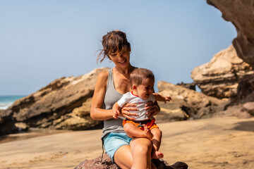 Portrait of a young mother with her crying baby by the sea in Playa de Garcey, west coast of Fuerteventura, Canary Islands. Spain