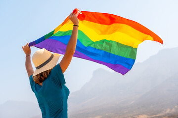 Lgbt symbol, a lesbian person in a green dress and a white hat with the rainbow flag in the desert