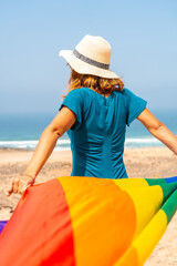 Lgbt symbol, an unrecognizable lesbian person with his back turned walking in a green dress and white hat waving the flag by the sea