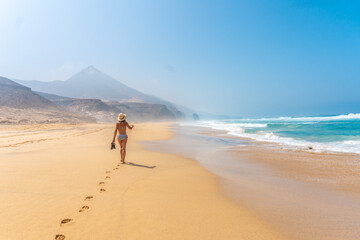 A young tourist walking alone on the wild beach Cofete in the natural park of Jandia, Barlovento coast, south of Fuerteventura, Canary Islands. Spain - obrazy, fototapety, plakaty