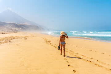 A young woman walking alone on the wild Cofete beach of the Jandia natural park, Barlovento coast, south of Fuerteventura, Canary Islands. Spain © unai