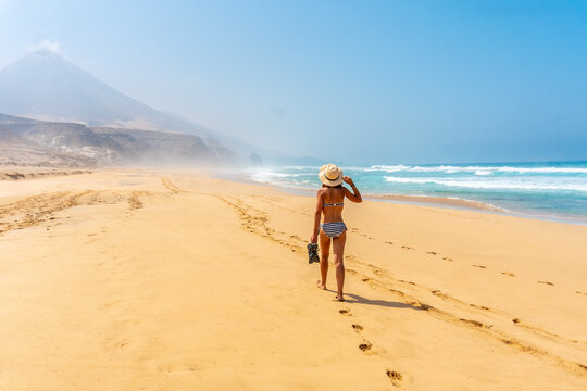 A young woman walking alone on the wild Cofete beach of the Jandia natural park, Barlovento coast, south of Fuerteventura, Canary Islands. Spain