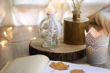 Old book with pressed autumn leaves, lit candles and vase with gypsophila flowers. Selective focus.