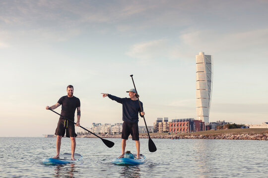 Male instructor talking with man while teaching to paddleboard in sea