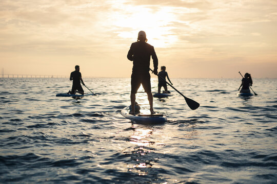 Women and man paddleboarding while spending leisure time in sea