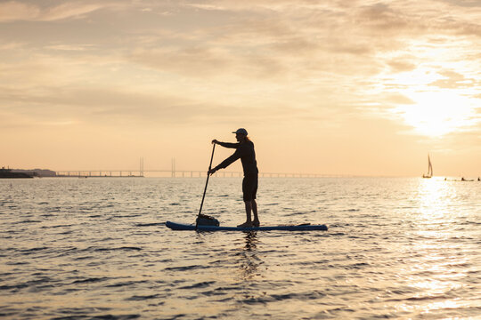 Side view of man rowing paddleboard in sea during sunset