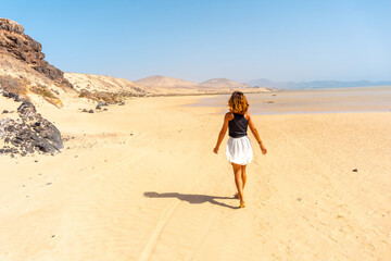 A young tourist walking along the Sotavento beach, ideal for sports such as Kitesurfing or sky surfing in the south of Fuerteventura, Canary Islands. Spain