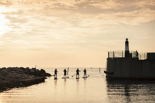 Female and male friends in sea by lighthouse during sunset