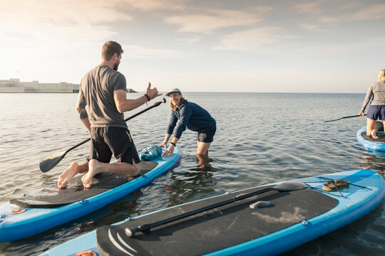 Man learning to paddleboard from male instructor in sea at beach