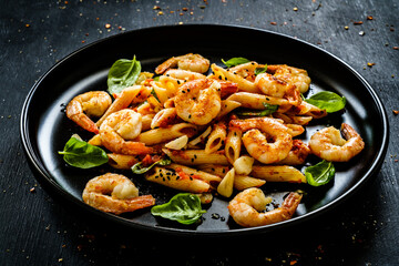 Penne with fried prawns in on black wooden background
