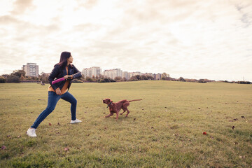Young woman throwing toy while playing with dog in public park