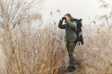 Wildlife photographer using telephoto lens with camouflage wild life using gimbal head on tripod. Wildlife photography with fast focusing. Professional photography equipment cinematic in the nature