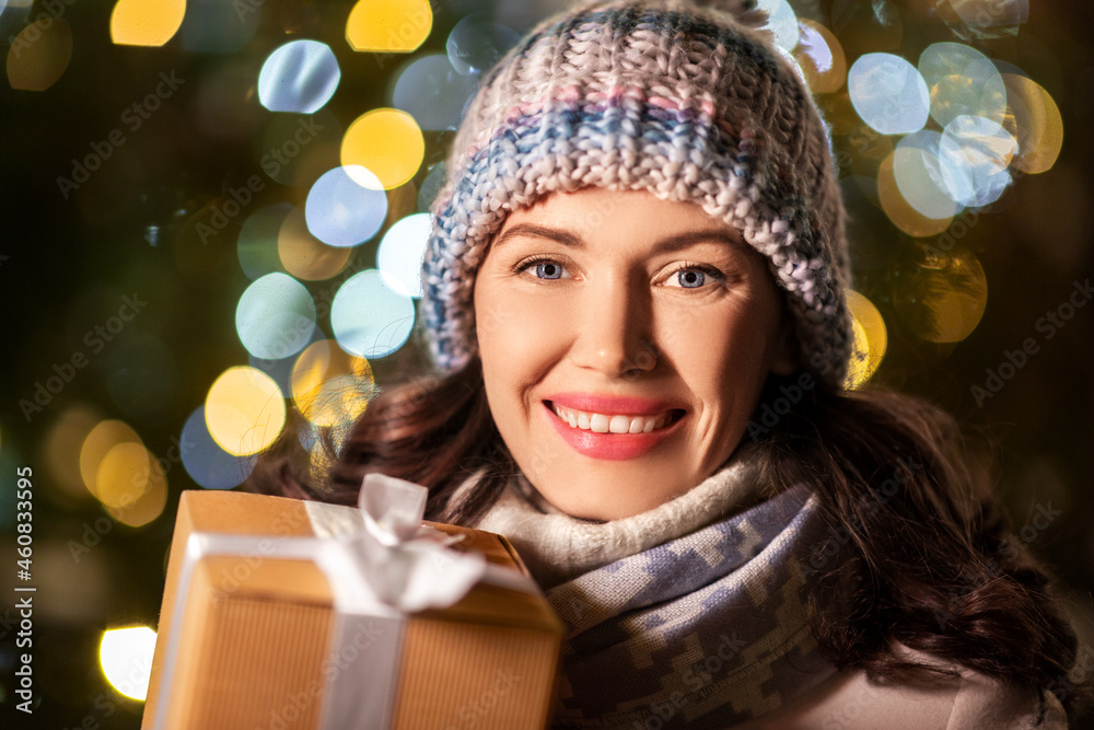 Wall mural winter holidays, celebration and people concept - happy smiling woman with christmas gift over festive lights