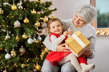 Fototapeta na wymiar christmas, holidays and family concept - happy grandmother and baby granddaughter with gift at home