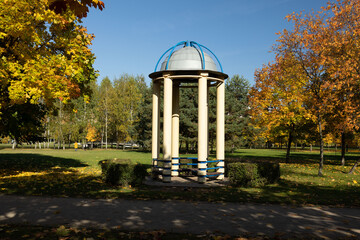 Autumn view, city park and modern buildings. Autumn orange trees and blue sky, resting alcove and...
