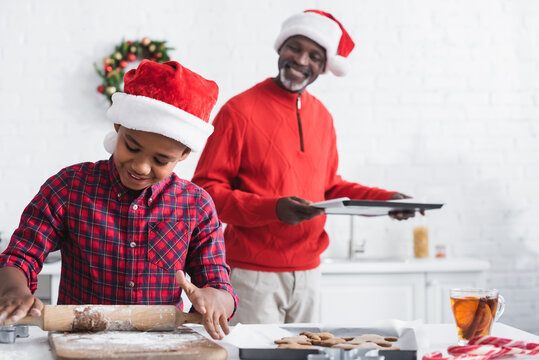 Blurred African American Man With Baking Sheet Near Boy Rolling Out Dough While Preparing Christmas Cookies