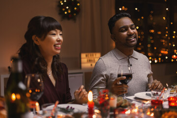 holidays, party and celebration concept - happy friends having christmas dinner at home and drinking wine